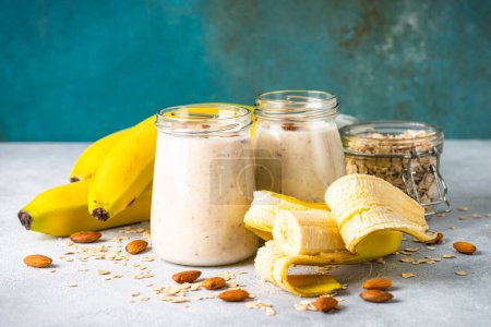 Foto de Almond banana smoothie with oat flakes in glass jars at white table. - Imagen libre de derechos
