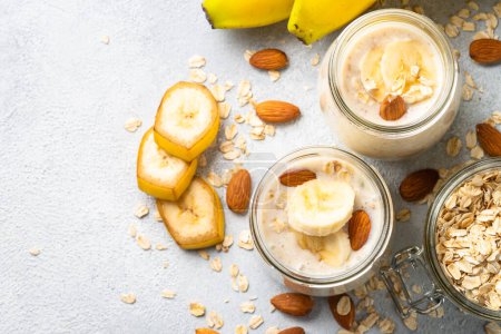 Foto de Almond banana smoothie with oat flakes in glass jars at white stone table. Top view. - Imagen libre de derechos