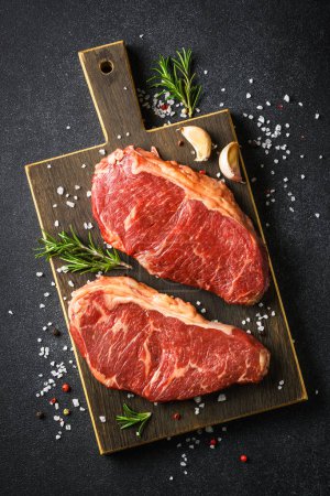 Foto de Beef steak with spices. Raw beef meat at black background. Vertical image. - Imagen libre de derechos
