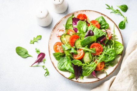 Foto de Salad from green leaves and vegetables. Fresh green salad in white plate. Top view. - Imagen libre de derechos