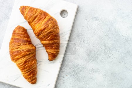 Téléchargez les photos : Croissant sur planche à découper à table blanche. Boulangerie française, vue de dessus. - en image libre de droit