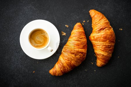 Téléchargez les photos : Croissant et tasse de café à fond noir. Pâtisserie française, boulangerie, petit déjeuner. Vue du dessus. - en image libre de droit