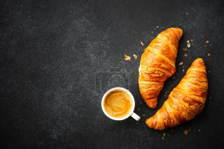 Croissant and cup of coffee at black background. Top view with copy space.