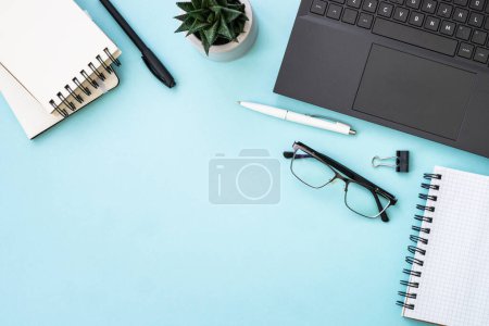 Photo for Office workspace with laptop, headphones, notepad and cactus. Flat lay image on blue with copy space. - Royalty Free Image