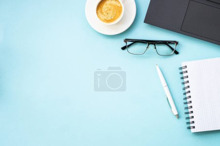 Foto de Office table desk with laptop, notepad, pen and cup of coffee. Flat lay on blue with copy space. - Imagen libre de derechos