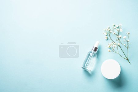 Téléchargez les photos : Natural cosmetic products at blue background. Cream, serum and white flowers. Flat lay image with copy space. - en image libre de droit