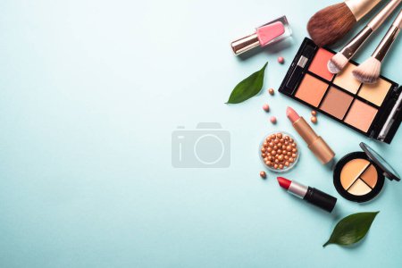 Foto de Make up professional cosmetics on blue background. Powder, lipstick, shadow, brushes with green leaves. Flat lay with copy space. - Imagen libre de derechos