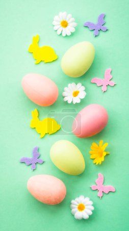 Photo for Easter background. Eggs, rabbit, spring flowers and butterfly. Flat lay at green background, vertical. - Royalty Free Image