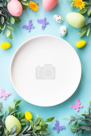 Photo for Easter table setting, Easter food background. White plate with eggs, spring flowers, green leaves and butterfly. Flat lay. - Royalty Free Image