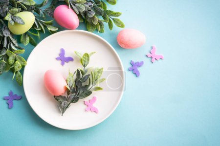 Photo for Easter table setting, Easter food background. White plate with eggs, spring flowers, green leaves and butterfly. Flat lay. - Royalty Free Image