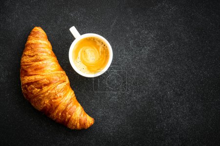 Téléchargez les photos : Croissant et tasse de café à fond noir. Pâtisserie française, boulangerie, petit déjeuner. Vue du dessus. - en image libre de droit