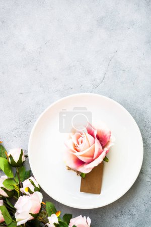 Téléchargez les photos : Table de printemps avec assiette blanche et fleurs roses. Décor de table pour un anniversaire ou un mariage. Vue de dessus à blanc. - en image libre de droit