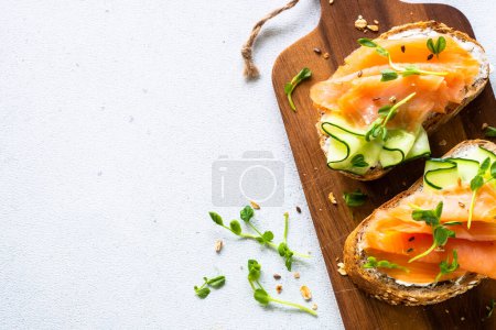 Foto de Sandwich abierto con queso crema, salmón y pepino. Vista superior en mesa blanca. - Imagen libre de derechos