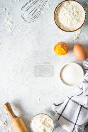 Baking background at light stone table. Flour, sugar, eggs and rolling pin. Top view with copy space.