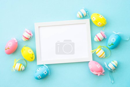 Téléchargez les photos : Fond de Pâques sur bleu. Œufs de Pâques colorés avec décorations et cadre blanc pour le texte. Pose plate avec espace de copie. - en image libre de droit