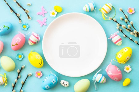 Foto de Mesa de Pascua, fondo de comida de Pascua. Plato blanco con huevos, flores y hojas verdes. Puesta plana. - Imagen libre de derechos