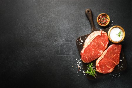 Téléchargez les photos : Viande de bœuf crue aux épices. Steaks de viande fraîche au tableau noir. Vue du dessus. - en image libre de droit