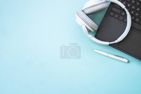 Photo for Laptop and wireless headphones on blue background. Flat lay with copy space. Podcast, listening, studying, music concept. - Royalty Free Image