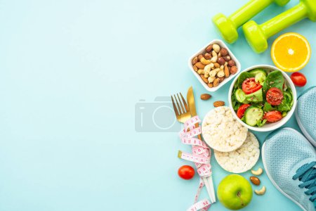 Healthy lifestyle and losing weight background. Sport shoes, dumbell and healthy food on blue. Flat lay with copy space.