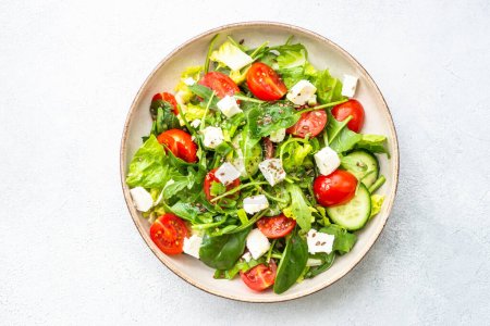 Photo for Green salad with spinach, arugula and tomatoes with olive oil. Top view on white. - Royalty Free Image