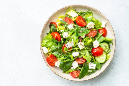 Photo for Spring salad in craft plate. Spinach, arugula, tomatoes and feta with olive oil. Top view on white. - Royalty Free Image