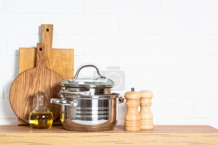 Foto de Kitchen table with kitchen utensils, cooking pots, oil bottle with wooden cutting board, white modern interior. - Imagen libre de derechos