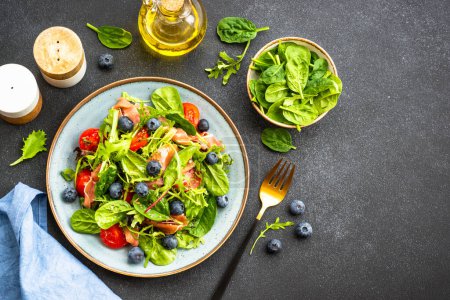 Téléchargez les photos : Salade saine au prosciutto, feuilles vertes mélangées et tomates sur fond sombre. Vue supérieure avec espace de copie. - en image libre de droit