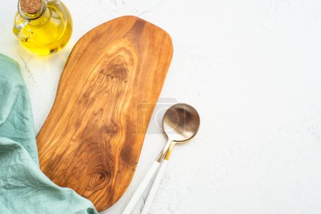 Olive board, olive oil, spoon and tablecloth on white kitchen table. Food background with copy space.