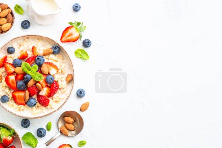 Photo for Oatmeal porrige with fresh berries and nuts on white background. Healthy breakfast, top view with copy space. - Royalty Free Image