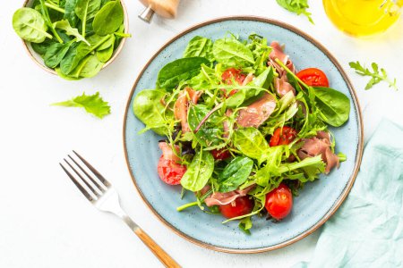 Photo for Green salad with fresh leaves, tomatoes and jamon at white table. Top view with copy space. - Royalty Free Image