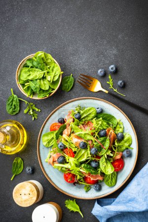 Téléchargez les photos : Salade saine au prosciutto, feuilles vertes mélangées et tomates sur fond sombre. Vue supérieure avec espace de copie. - en image libre de droit