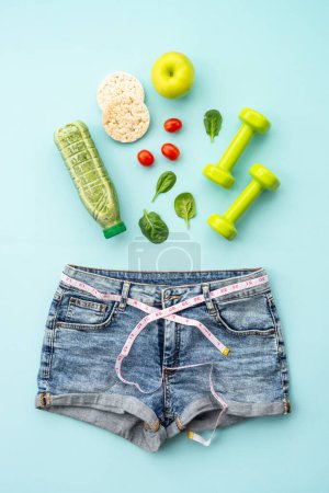 Téléchargez les photos : Perdre du poids fond. Haltères, aliments sains et jeans avec ruban à mesurer. Pose plate sur bleu. - en image libre de droit