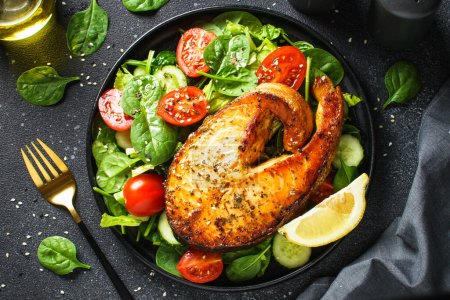 Téléchargez les photos : Bifteck de saumon et salade verte fraîche sur fond noir. Régime alimentaire Keto, des aliments sains. Régime méditerranéen. - en image libre de droit