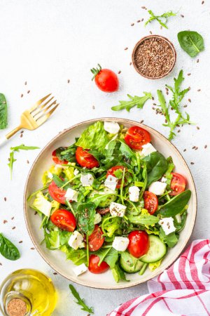 Photo for Spring salad in craft plate. Spinach, arugula, tomatoes and feta with olive oil. Top view, vertical on white. - Royalty Free Image