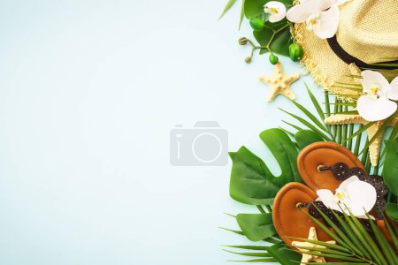 Photo for Summer vacation and travel concept. Palm leaves, hat and sandals on blue background. Flat lay with copy space. - Royalty Free Image