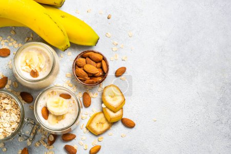Téléchargez les photos : Almond banana smoothie with oat flakes in glass jars at white stone table. Top view. - en image libre de droit
