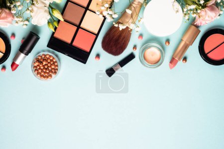 Foto de Make up professional, Cosmetic products on blue background. Cream, powder, shadow, brushes with green leaves and flowers. Top view with copy space. - Imagen libre de derechos