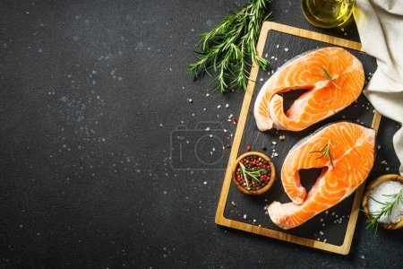 Photo for Salmon steaks on cutting board at black background. Top view with ingredients for cooking. - Royalty Free Image
