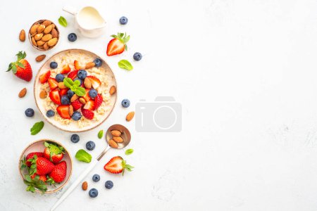 Photo for Oatmeal porrige with fresh berries and nuts on white background. Healthy breakfast, top view with copy space. - Royalty Free Image