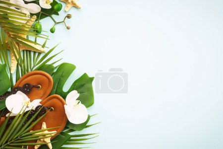 Photo for Summer vacation and travel concept. Palm leaves, flowers and sandals on blue background. Flat lay with copy space. - Royalty Free Image
