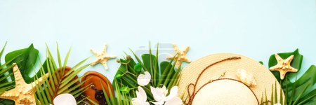 Téléchargez les photos : Tissu d'été et accessoires. Feuilles de palmier, chapeau, sandales et fleurs sur fond bleu. Format de bannière longue. - en image libre de droit