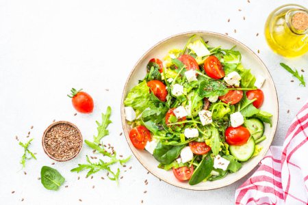Téléchargez les photos : Salade verte aux épinards, roquette, tomates et feta à l'huile d'olive. Vue de dessus sur blanc. - en image libre de droit