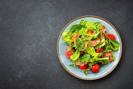 Téléchargez les photos : Salade verte aux feuilles fraîches, tomates et jamon à table noire. Vue supérieure avec espace de copie. - en image libre de droit