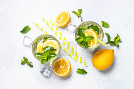 Téléchargez les photos : Citronnade en verre sur table blanche avec citrons frais et menthe. Boisson froide d'été vue du dessus. - en image libre de droit