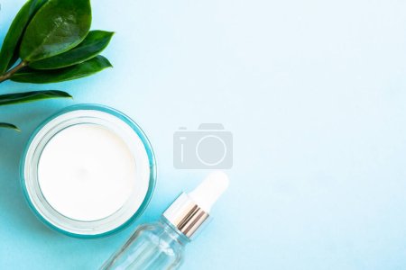 Photo for Natural cosmetic, cream jar with green leaves on blue. Flat lay with copy space. - Royalty Free Image