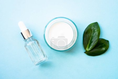 Photo for Natural cosmetic products on blue. Cream and serum bottlr with green leaves. Flat lay, minimal. - Royalty Free Image