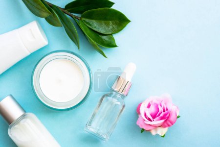 Photo for Natural cosmetic products flat lay on blue. Cream, serum, tonic with green leaves and flowers. - Royalty Free Image
