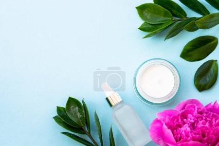 Photo for Natural cosmetic products flat lay on blue. Cream and serum with green leaves and flowers. - Royalty Free Image