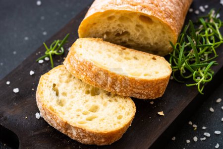 Photo for Italian Ciabatta bread on wooden board on black background. Close up. - Royalty Free Image