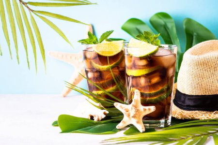 Foto de Cuba Libre bebida helada, alcohólica con hojas de palma y conchas marinas. Vacaciones tropicales. - Imagen libre de derechos